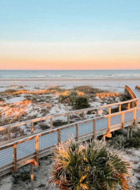 This image shows New Smyrna Beach during a vibrant sunset, with calm waves and golden sand. Surfers and beachgoers enjoy the relaxing atmosphere of this beautiful shoreline.