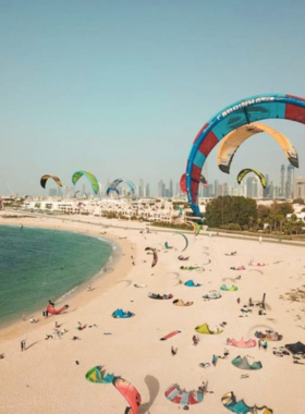 This image shows Kite Beach in Dubai, where visitors enjoy activities like kitesurfing, paddleboarding, and sunbathing along a pristine coastline.