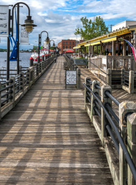 This image shows the picturesque Riverwalk in Wilmington, NC, offering a scenic view of the Cape Fear River with people strolling along the boardwalk, enjoying the beautiful waterfront.