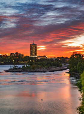 This image shows the Arkansas River at sunset in Tulsa, with calm waters reflecting the orange and pink hues of the evening sky.