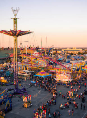 This image shows the Tulsa State Fair at night, with colorful lights illuminating rides, games, and crowds enjoying the festive atmosphere.