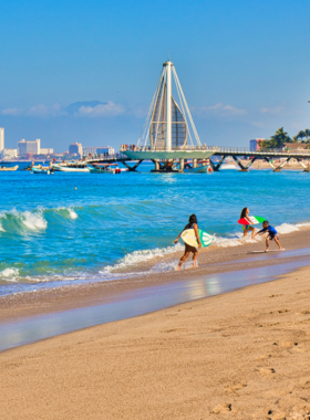 This image shows a lively beach scene at Playa de los Muertos in Puerto Vallarta, with people sunbathing on the sandy shore, enjoying clear blue waters, and participating in water activities like parasailing.