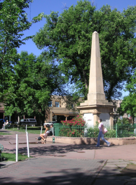 This image shows the historic Santa Fe Plaza, surrounded by adobe buildings with art galleries, shops, and restaurants, capturing the vibrant cultural center of Santa Fe.