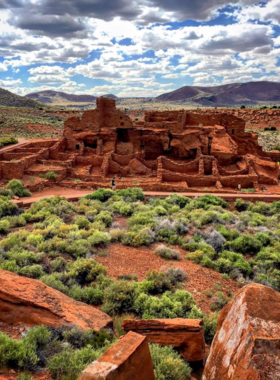 This image shows the well-preserved red sandstone ruins of Wupatki Pueblo, standing tall against the backdrop of a desert landscape and blue sky.