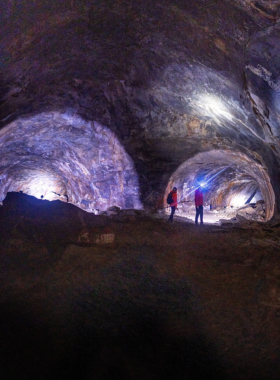 This image shows adventurers exploring the Lava River Cave, with flashlights illuminating the dark interior and rugged lava tube formations.
