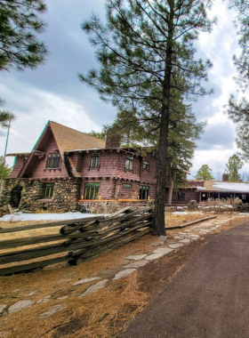 This image shows the historic Riordan Mansion, a large Arts and Crafts-style home surrounded by manicured lawns and tall pine trees.