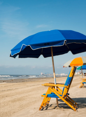 This image shows families enjoying the sun at Stewart Beach, with people relaxing on beach chairs, children playing in the sand, and the calm waves of the Gulf of Mexico in the background.