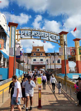  This image shows the lively atmosphere at the historic Pleasure Pier, with people riding the Ferris wheel, playing carnival games, and enjoying the ocean views at sunset on the iconic pier.