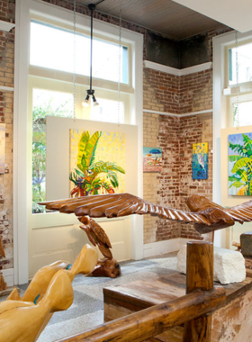 This image shows visitors admiring vibrant works of art at a local gallery in Galveston, with paintings and sculptures on display in a cozy, welcoming atmosphere.