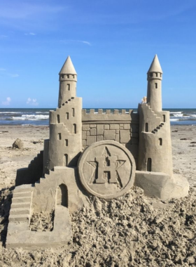 This image shows impressive sandcastle sculptures at a competition on Galveston Beach, with artists working on their creations while spectators watch in awe under the bright sky.