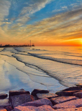  This image shows a beautiful sunset over Galveston Beach, with the sun casting golden hues over the calm ocean waves and people enjoying the tranquil atmosphere on the sand.
