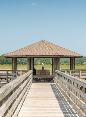 This image shows a replica of a historical home at Mitchelville Freedom Park, surrounded by trees and accompanied by informative signs.

