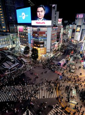 This image shows the bustling Shibuya Crossing during rush hour in Tokyo, with hundreds of pedestrians moving in all directions. Bright billboards and city lights surround the iconic intersection, creating a vibrant urban scene.
