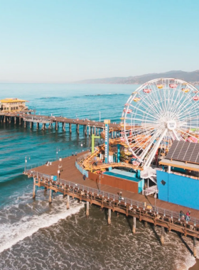 This image shows the Santa Monica Pier with its Ferris wheel at sunset and the golden beach, ideal for fun and relaxation.