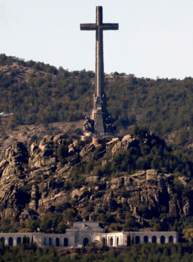 This image shows the Valle de los Caídos, a monumental site in Madrid dedicated to the victims of the Spanish Civil War, featuring a towering cross and a basilica in the mountains.