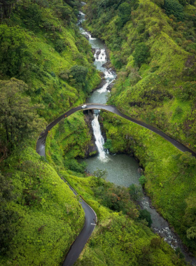 This image shows the stunning view of one of the many waterfalls along the famous Road to Hana in Maui. The waterfall cascades over the rocks, surrounded by lush greenery, providing a peaceful and picturesque landscape for travelers.