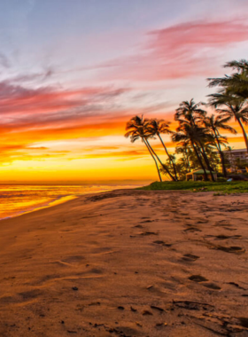 This image shows the peaceful Ka'anapali Beach during sunset, with the sky painted in vibrant orange and pink hues. The clear waters gently lap against the golden sand, creating a serene and beautiful atmosphere for visitors.