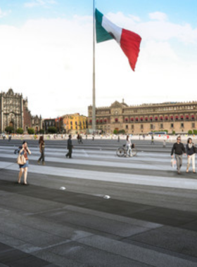  This image shows the bustling Zócalo square with a giant Mexican flag in the center, surrounded by historical landmarks like the National Palace and Metropolitan Cathedral. Crowds gather for events, capturing the lively essence of Mexico City’s culture.