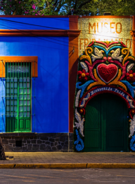  This image shows Museo Frida Kahlo, a vibrant blue house in Coyoacán with lush gardens and a courtyard. Visitors are seen exploring the historic residence, showcasing Frida Kahlo’s life, her artwork, and personal memorabilia.