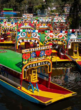 This image shows the vibrant Xochimilco canals with colorful gondola-like boats called trajineras. Musicians play traditional tunes, and visitors enjoy festive rides surrounded by greenery and lively cultural ambiance.