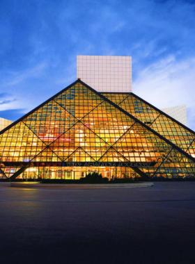 This image shows the exterior of the Rock & Roll Hall of Fame in Cleveland, with its iconic glass pyramid design, celebrating the history and culture of rock music.