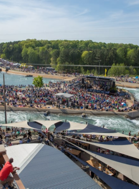 This image shows a group of people enjoying an exciting rafting experience at the Whitewater Center, surrounded by rushing water and lush green landscapes. The thrill of the rapids is evident as adventurers work together to navigate through the water.