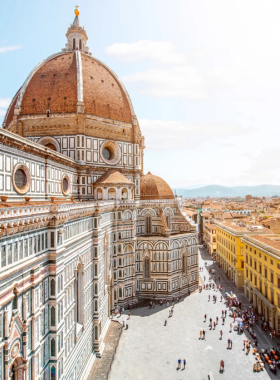 This image shows the breathtaking panoramic view from the top of the Duomo in Florence. The dome's intricate design and the city’s skyline, including the Arno River and historic buildings, are visible.