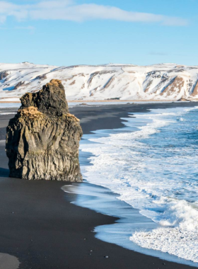 This image shows the dramatic black sand beach of Reynisfjara in Iceland, with towering basalt columns and powerful ocean waves, a must-see natural wonder along the coast.