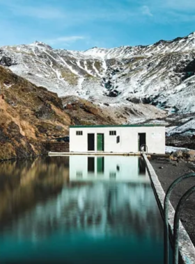 This image shows the hidden geothermal pool, Seljavallalaug, in Iceland, nestled in a peaceful valley surrounded by mountains, offering visitors a secluded and relaxing swimming experience.