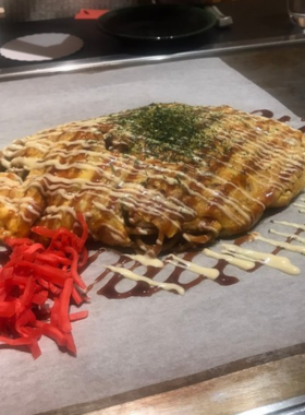 This image shows a plate of freshly made okonomiyaki at Fukutaro restaurant in Osaka. The savory pancake, filled with various ingredients such as pork and seafood, is a beloved local dish that represents Osaka’s culinary heritage.