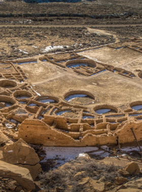 This image shows the ruins of Pueblo Bonito at Chaco Culture National Historical Park, a UNESCO World Heritage Site. Visitors are seen walking through the impressive ancient ruins, exploring the fascinating history of the Ancestral Puebloans.