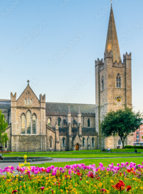 This image shows St. Patrick's Cathedral, Ireland's largest and oldest cathedral, featuring magnificent Gothic architecture, tall spires, and colorful stained glass windows. Visitors are seen exploring the church's peaceful interiors and surrounding garden park.