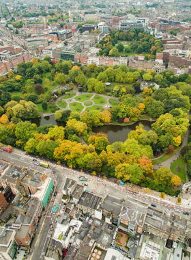 This image shows St. Stephen’s Green, a peaceful Victorian-style park in Dublin with colorful flowerbeds, a pond with ducks, and walking paths lined with benches. People are relaxing, having picnics, and enjoying the park’s natural beauty.