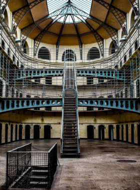 This image shows the historic Kilmainham Gaol in Dublin, with its stone walls, narrow prison cells, and iron staircases. Visitors are seen on a guided tour, learning about the stories of revolutionaries and political prisoners who were once held here.