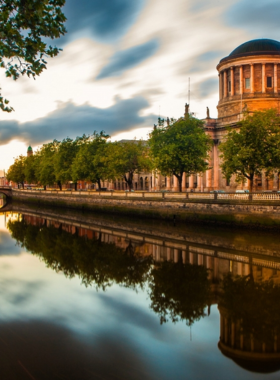 This image shows the River Liffey flowing through Dublin city, with iconic bridges like the Ha’penny Bridge in view. People are walking along the riverside paths, enjoying beautiful reflections and scenic city landscapes.