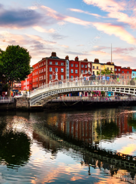 This image shows the historic Ha’penny Bridge in Dublin, with its beautiful iron arches and pedestrians walking across. The bridge reflects on the River Liffey below, surrounded by lively cityscapes and sunset hues.