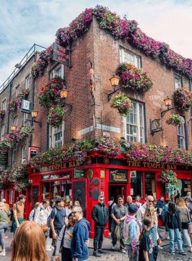 This image shows Temple Bar, Dublin’s cultural and nightlife hub, with its cobblestone streets, colorful pubs, and lively crowds. Musicians are performing live, and people are enjoying food, drinks, and vibrant entertainment.