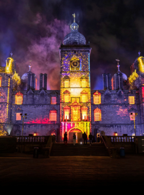 This image shows a vibrant scene from the Edinburgh Festival Fringe, with street performers, colorful decorations, and lively crowds celebrating music, art, theater, and cultural performances.