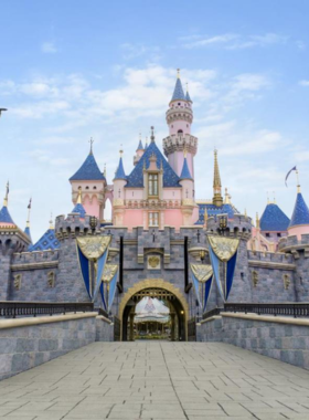 This image shows the Sleeping Beauty Castle at Disneyland Resort in Anaheim, California. The vibrant castle stands tall, surrounded by happy visitors enjoying their day. Bright blue skies, colorful decorations, and excited families reflect the magical atmosphere. The castle, adorned with beautiful details, is the centerpiece of the theme park. People are taking photos, smiling, and walking towards fun rides and attractions in the park