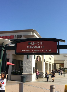 This image shows the luxurious South Coast Plaza mall in Costa Mesa, featuring shoppers walking past high-end stores. The scene includes elegant architecture, bright store windows, and decorative lighting. People carry shopping bags while others enjoy sitting at cozy café corners. The mall’s interior reflects a mix of style and comfort, capturing Costa Mesa’s upscale shopping experience. The image highlights the lively and bustling atmosphere of this shopping hub.