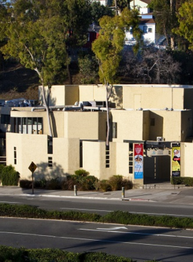 This image shows a live theatrical performance at the Laguna Playhouse. The stage is beautifully lit with colorful lights, and actors are seen performing in front of an audience. The cozy theater seats are filled with people watching attentively. The image highlights the intimate setting, talented performers, and vibrant cultural experience at Laguna Playhouse. The actors’ expressive gestures and scenic backdrops add to the artistic atmosphere of the theater.