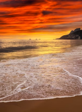 This image shows Ipanema Beach in Rio de Janeiro, with golden sand, beachgoers playing sports, and the Dois Irmãos mountains in the background. The lively beach scene captures the essence of Rio’s culture and beauty.