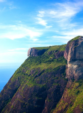 This image shows the stunning view from the top of Pedra da Gávea, overlooking Rio de Janeiro’s mountains, beaches, and city below. A hiker stands at the peak, celebrating the challenging climb and breathtaking scenery.