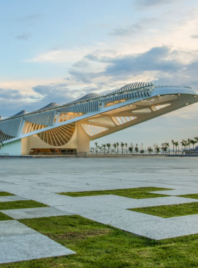 This image shows the futuristic Museum of Tomorrow, with its unique modern architecture surrounded by water. Visitors can be seen walking around, enjoying the exhibits and reflecting on global sustainability and innovation themes.