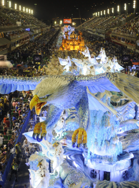 This image shows the vibrant Rio Carnival parade, with samba dancers in colorful costumes, large floats, and an energetic crowd cheering. The dazzling lights and music highlight the cultural celebration’s festive spirit.