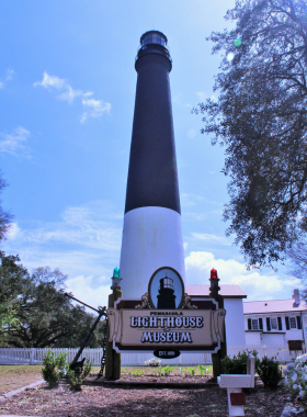 This image shows the iconic Pensacola Lighthouse standing tall against a blue sky. Visitors can climb the 177 steps to the top for breathtaking views of Pensacola Bay and its surrounding waters. The lighthouse is a key historical landmark, guiding ships and sailors for over 160 years.