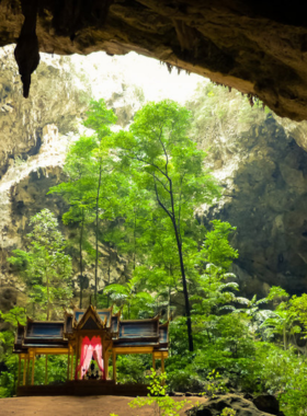 This image shows sunlight streaming through the opening of Phraya Nakhon Cave in Thailand, illuminating a royal pavilion inside. The natural light creates a magical, serene atmosphere, perfect for nature and adventure photography.