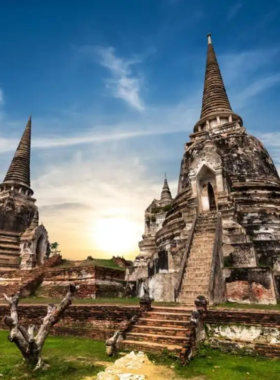 This image shows the ruins of an ancient temple in Ayutthaya, with towering chedis and a reclining Buddha. The warm colors of the sunset create a magical glow over the historic architecture, offering a glimpse into Thailand's rich past.