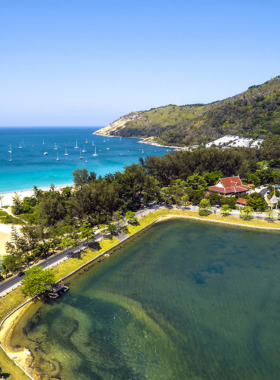 This image shows the peaceful Nai Harn Beach, with calm waters and people swimming or lounging on the beach. The surrounding greenery and scenic views add to the tranquil vibe, offering a peaceful escape for visitors looking for relaxation away from the busy crowds.