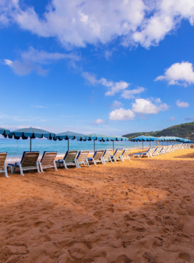 This image shows the expansive Karon Beach with clear waters and people enjoying various water sports like snorkeling and windsurfing. The long stretch of golden sand provides a perfect spot for both relaxation and adventure, attracting beach lovers of all kinds.